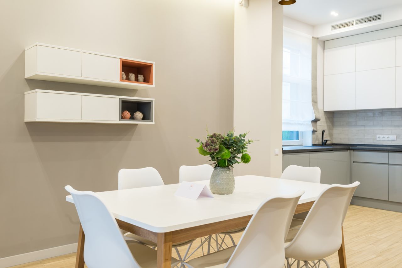 services-02 White table with green flowers and chairs placed near kitchen counter with cabinets in modern apartment with shelves and decorations